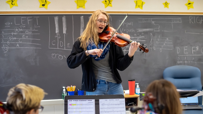 A music teacher teaches while playing a violin. 