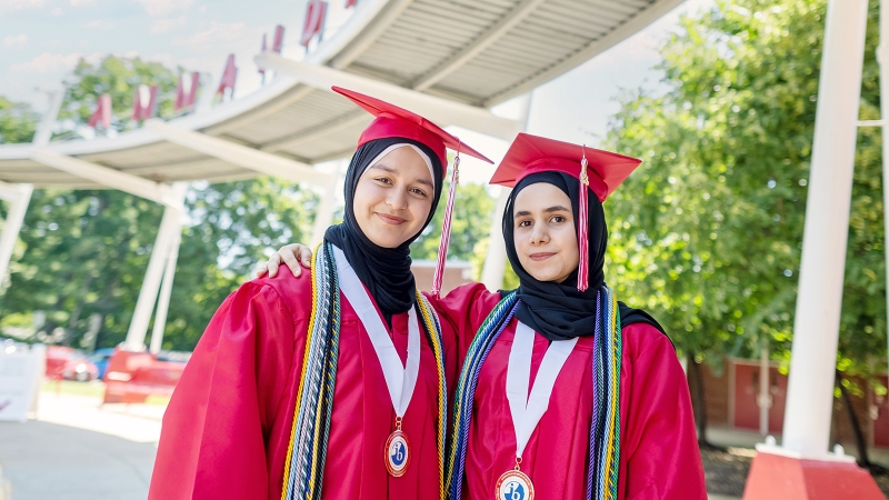 Founders of a club to help refugees, Sosan Barakzai and Husna Basiri, wear a cap, gown and International Baccalaureate candidate medals as they prepare to graduate from Annandale High School.