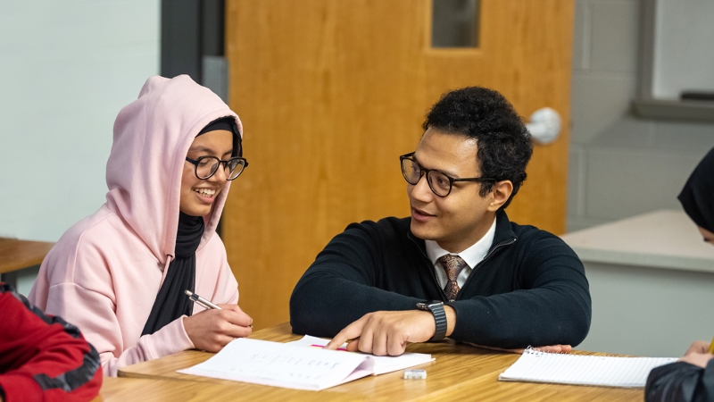 A Justice High School Arabic language instructor confers with a student at her desk.