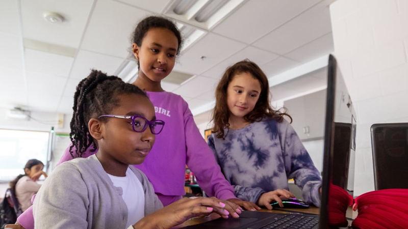 three elementary school girls looking at laptop