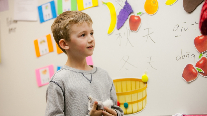 Student in front of bulletin board with Chinese words and characters.