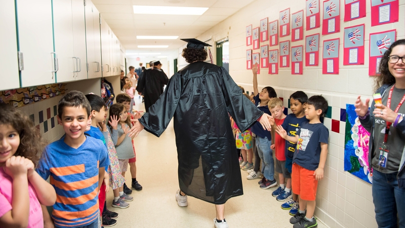 graduate high fiving elementary students in the hallway