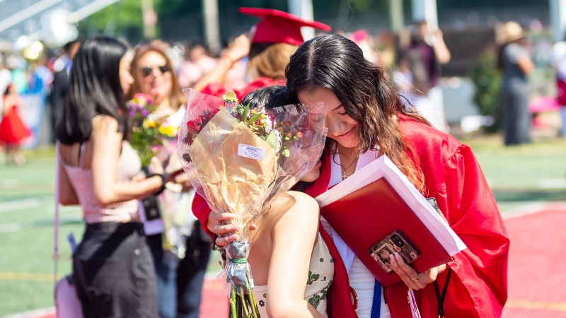 Graduating student hugging another person.