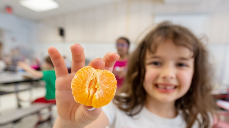 girl holding up a peeled orange