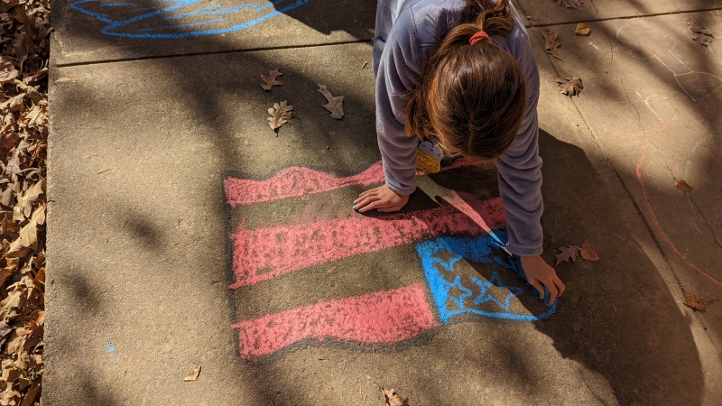 An Orange Hunt Elementary student uses chalk to draw a picture of the U.S. flag during Veterans Day celebrations.