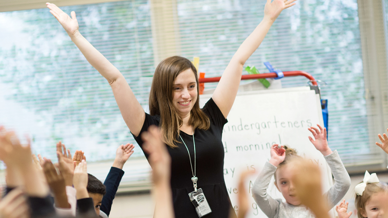 Teacher with her hands up and students with their hands up