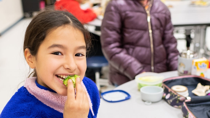 student eating a piece of broccoli