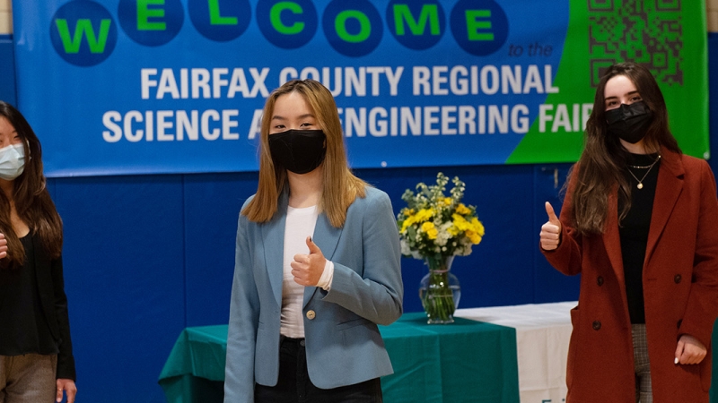 three girls in front of science fair banner