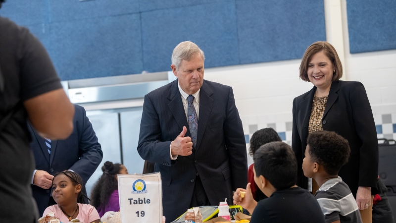 USDA Chief Tom Vilsack and Annandale Terrace ES Principal Ingrid Badia chat with students in the school cafeteria.