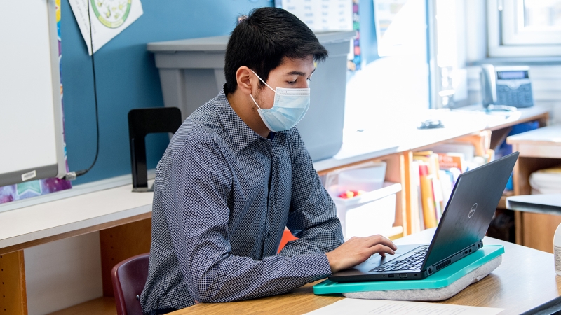 male student wearing mask and working at a laptop computer