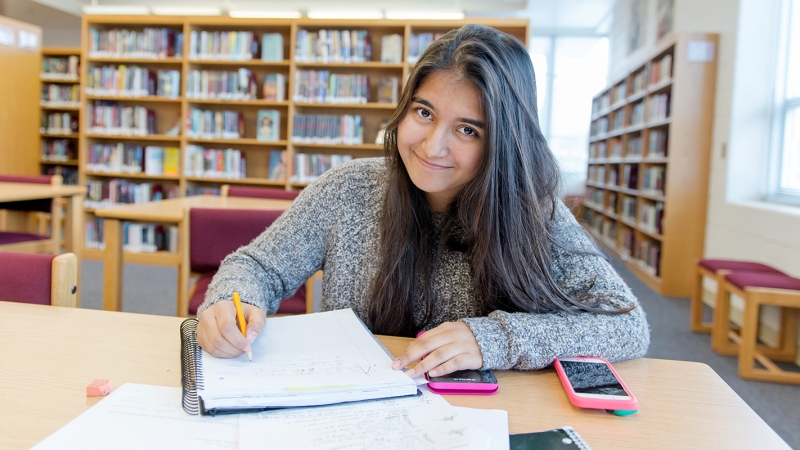 Photo of a female student doing homework at a table in the library