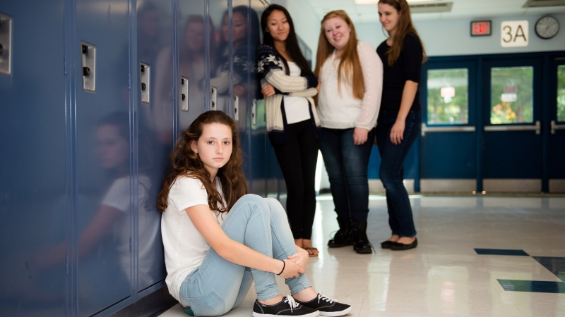 Photo of a female student sitting beside a locker while three other students stand behind her.