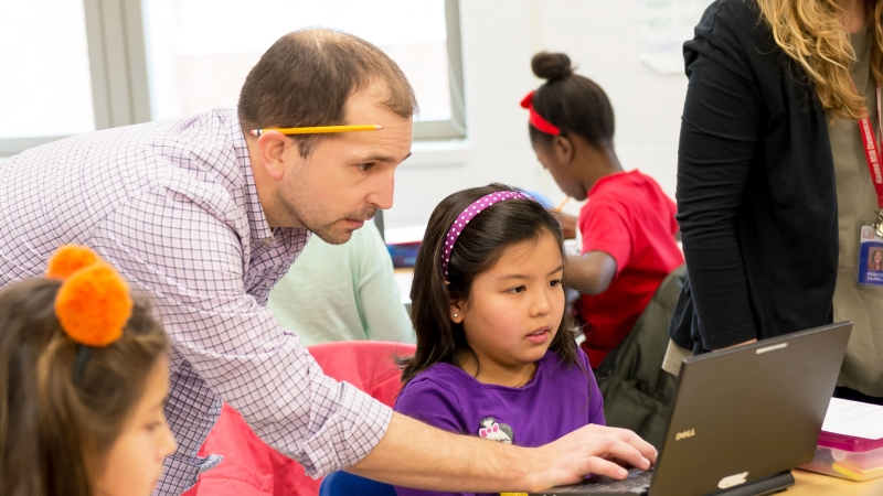 elementary school teacher helping student with a computer