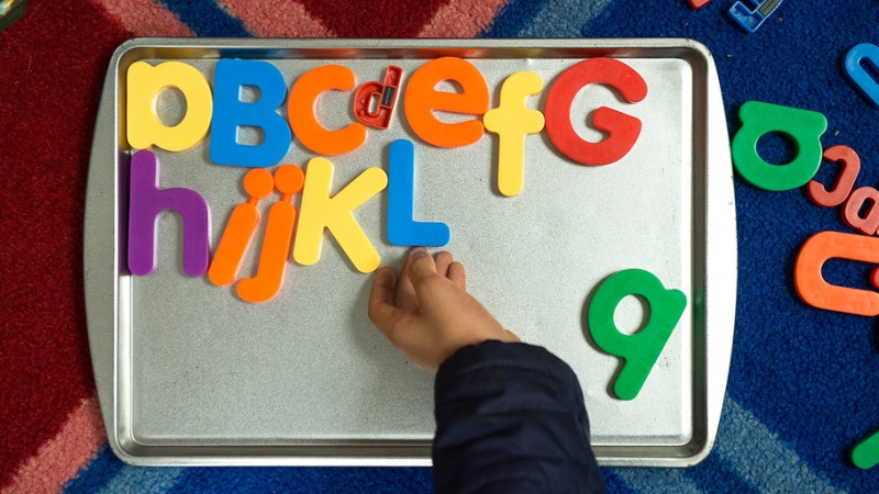 child moving magnetic letters on a metal tray