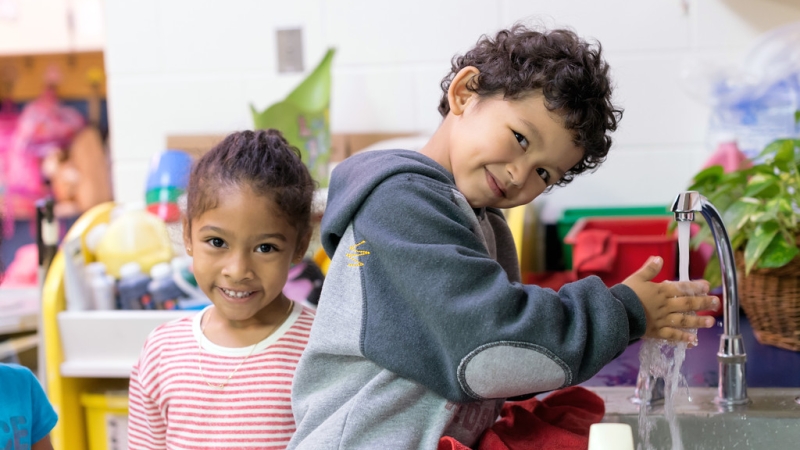 photo of a little boy washing his hands and a girl standing near the sink