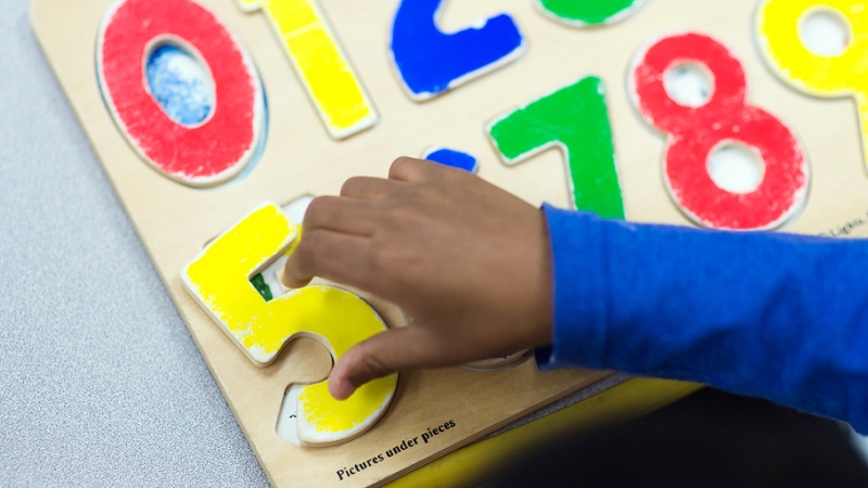 a child's hand playing with a wooden number puzzle