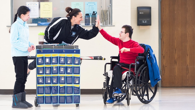 a student in a wheelchair giving a teacher a high five 