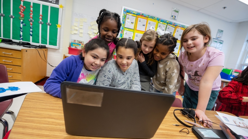 six elementary students looking at a laptop screen