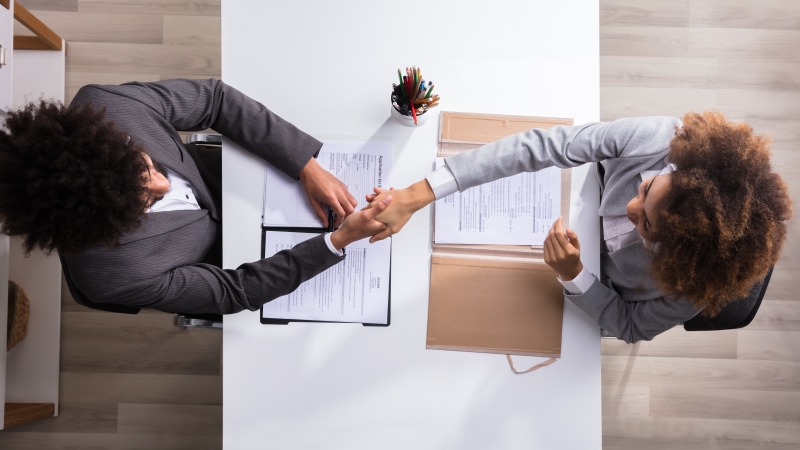two people shaking hands over documents on a desk