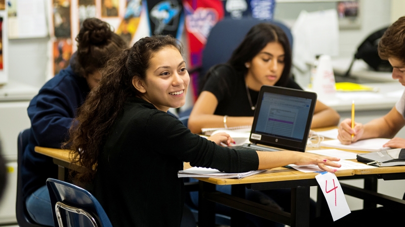 Photo of a female student sitting a her desk with a laptop in front of her