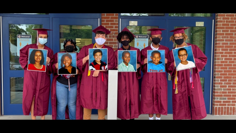 photo of high school grads in cap and gown displaying photos of themselves in elementary school 