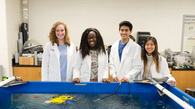 Four students in front of a large floor watertank