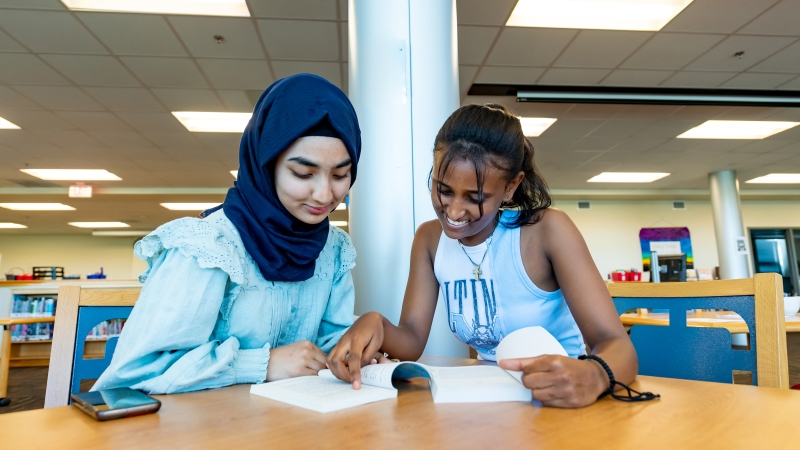 Two female students reading books at a table in the library