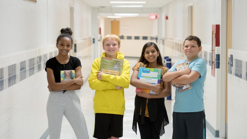 Four students holding books standing in a school hallway