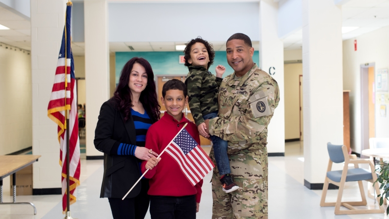 Photo of a family with a mother, two children, and the father who is wearing a military uniform.