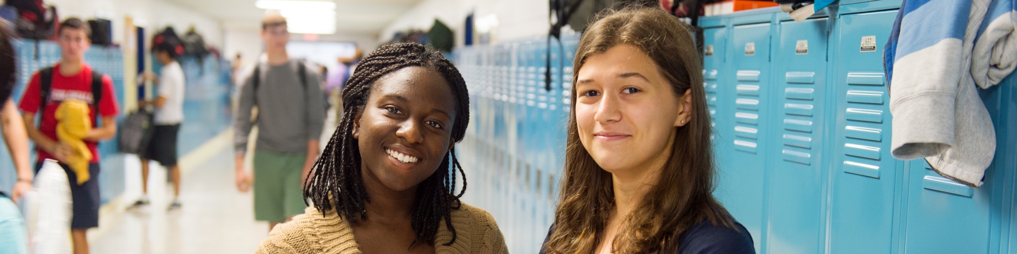 two female students standing in front of blue lockers in a school hallway