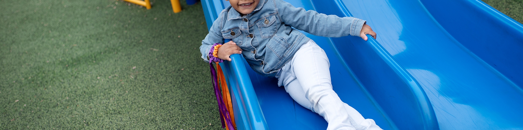 Female student sitting at the bottom of a blue slide smiling
