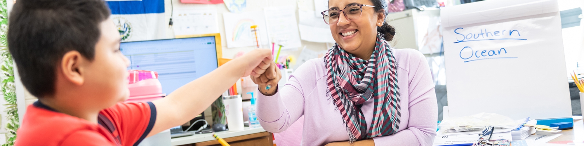 Teacher working with student at teacher desk bumping fists in celebration