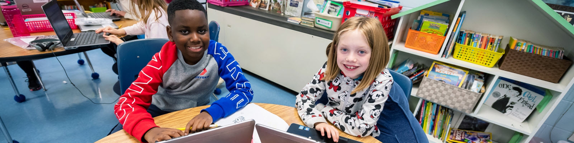 two elementary school students working at desk with laptops