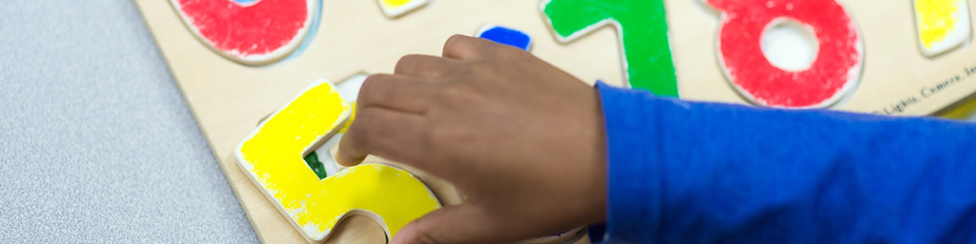 a child's hand holding a number 5 puzzle piece