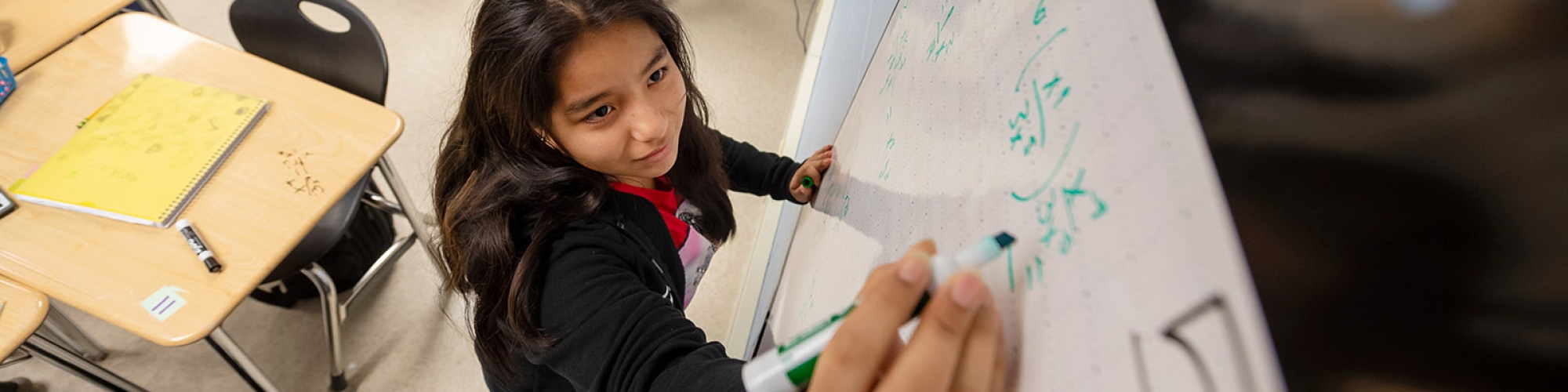 middle school student writing on a dry erase board.