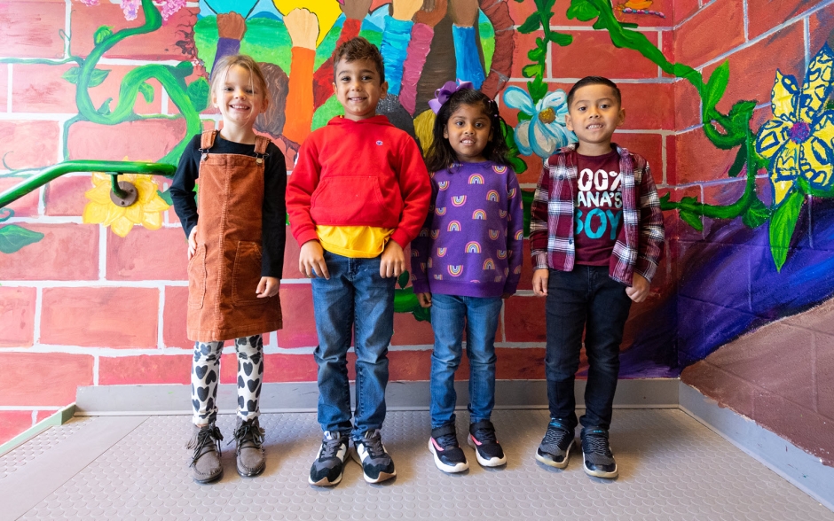 four children standing in front of a mural in a school building