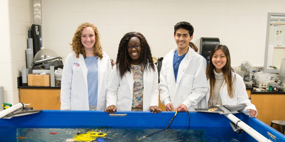 Four students in front of a large floor watertank