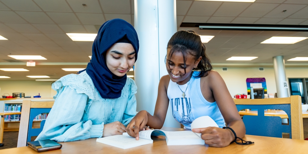 Two female students reading books at a table in the library